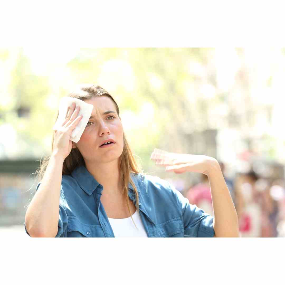 sweaty hot skin can cause heat rash. sweaty woman wiping her forehead on a hot day